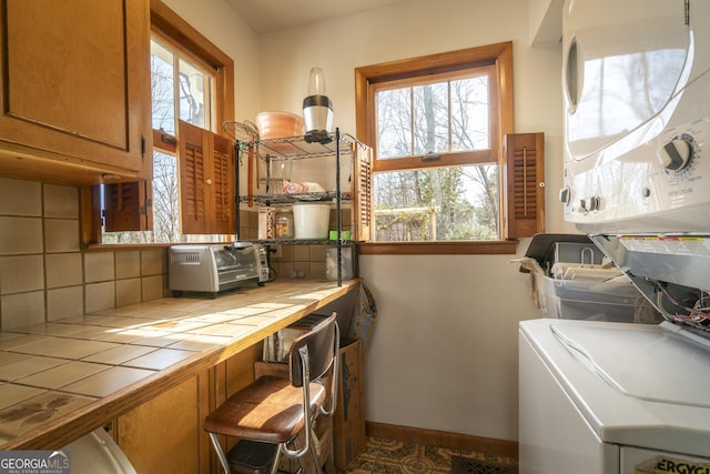 washroom featuring cabinet space, a toaster, baseboards, and stacked washer / dryer