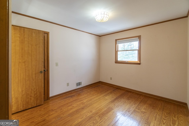 spare room with baseboards, light wood-style flooring, visible vents, and crown molding