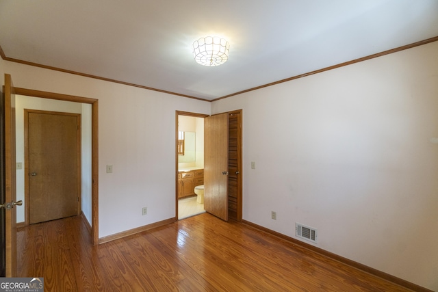 unfurnished bedroom with ensuite bathroom, visible vents, baseboards, light wood-style floors, and ornamental molding