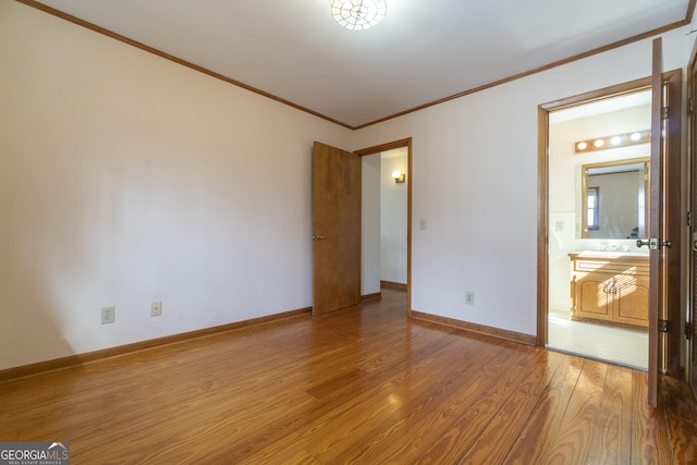 unfurnished bedroom featuring baseboards, ensuite bathroom, wood finished floors, and crown molding