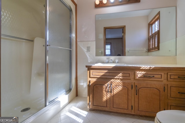 bathroom with toilet, vanity, tile walls, tile patterned floors, and a stall shower