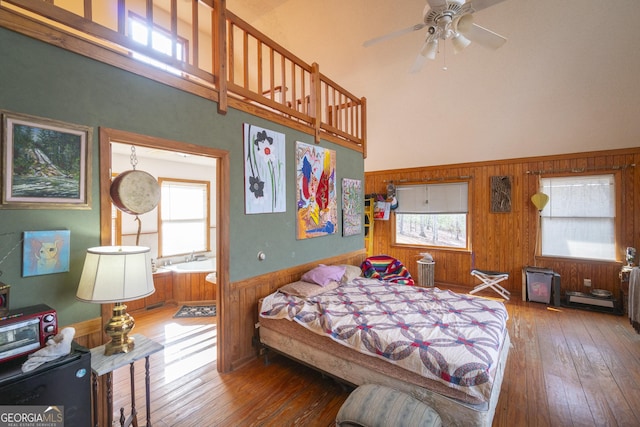 bedroom featuring a wainscoted wall, wood walls, a towering ceiling, and hardwood / wood-style flooring