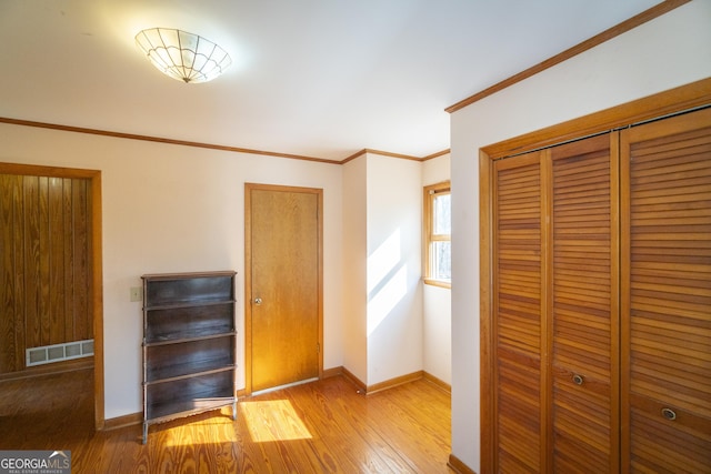 unfurnished bedroom featuring wood finished floors, visible vents, baseboards, a closet, and crown molding