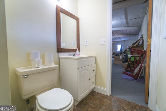 half bathroom featuring stone finish flooring, baseboards, vanity, and toilet