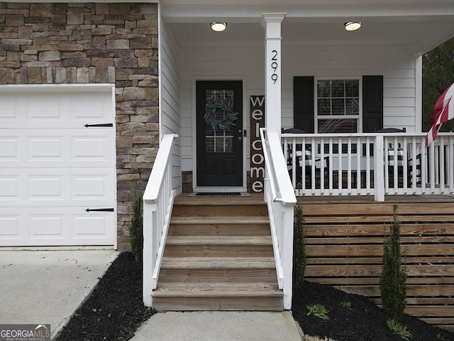 doorway to property with stone siding, a porch, and a garage