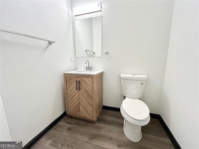 half bath featuring baseboards, vanity, toilet, and wood finished floors