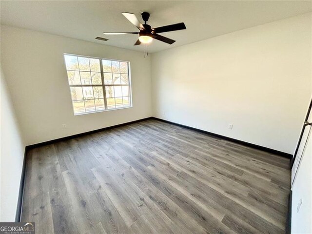 spare room featuring a ceiling fan, visible vents, baseboards, and wood finished floors