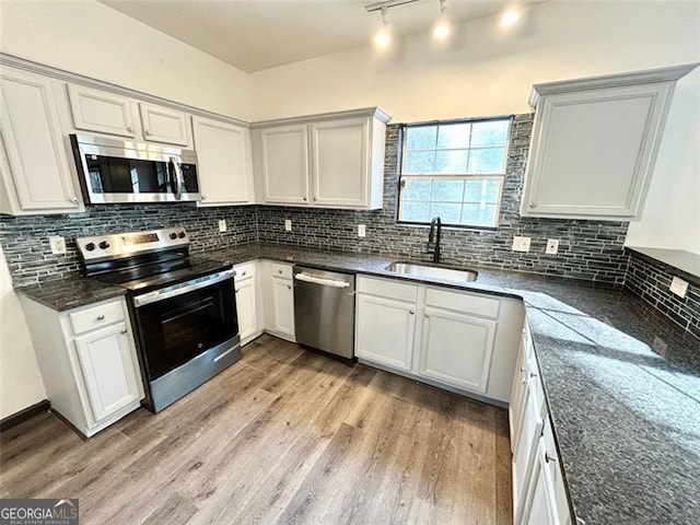 kitchen featuring light wood finished floors, tasteful backsplash, appliances with stainless steel finishes, dark stone countertops, and a sink