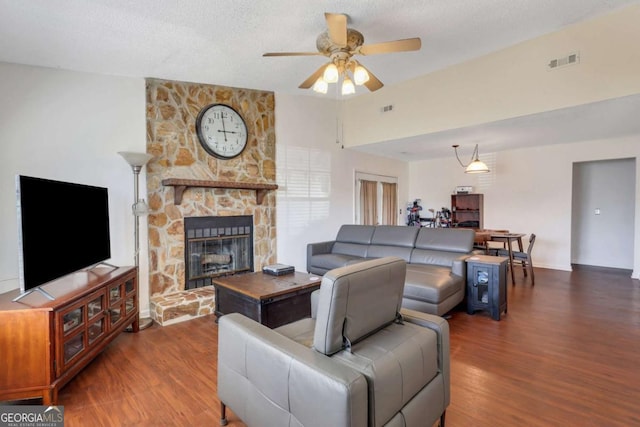 living room featuring visible vents, a ceiling fan, a stone fireplace, a textured ceiling, and wood finished floors