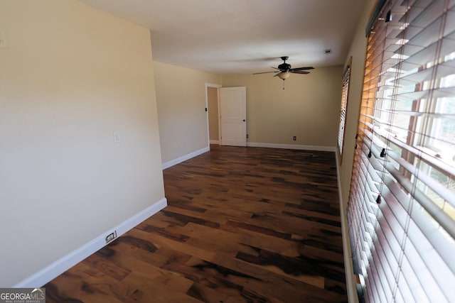 empty room with ceiling fan, dark wood-type flooring, and baseboards