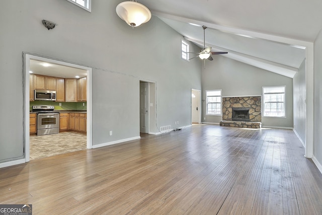 unfurnished living room with visible vents, light wood-style flooring, ceiling fan, a stone fireplace, and baseboards