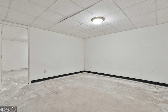 finished basement featuring a paneled ceiling, concrete block wall, and baseboards