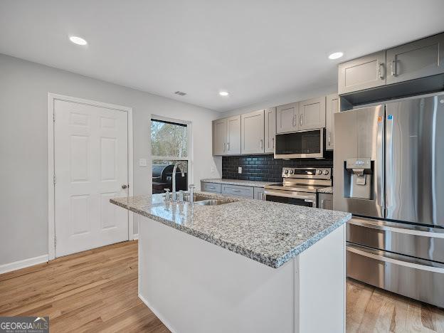 kitchen featuring gray cabinetry, a sink, stainless steel appliances, light wood finished floors, and decorative backsplash