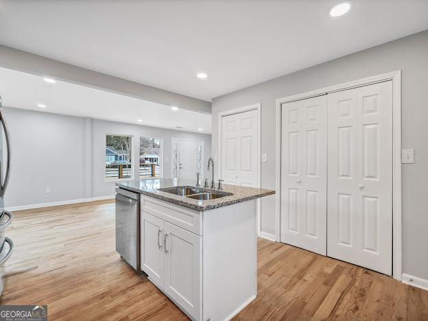 kitchen with light stone counters, a sink, white cabinets, dishwasher, and light wood-type flooring