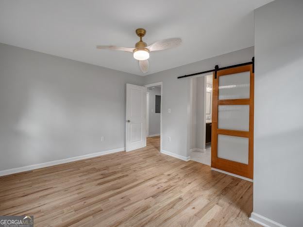 unfurnished bedroom with a barn door, baseboards, light wood-style floors, and ceiling fan