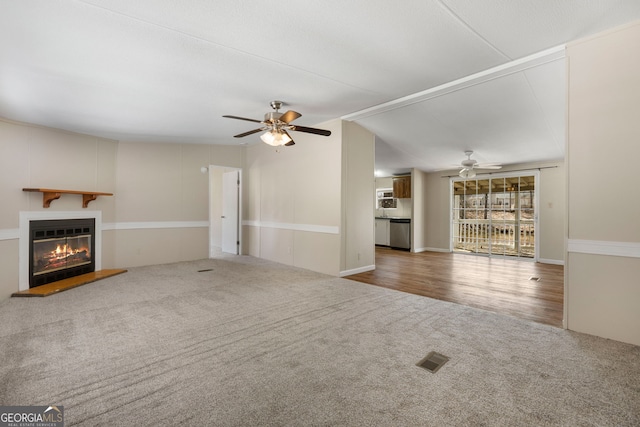 unfurnished living room with ceiling fan, carpet floors, visible vents, vaulted ceiling, and a glass covered fireplace