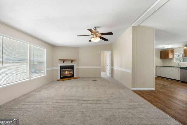 unfurnished living room featuring a sink, wood finished floors, a glass covered fireplace, and a ceiling fan