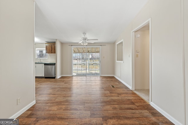 unfurnished living room featuring a healthy amount of sunlight, baseboards, a ceiling fan, and dark wood-type flooring