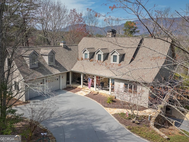 cape cod home with driveway, a garage, a chimney, roof with shingles, and covered porch