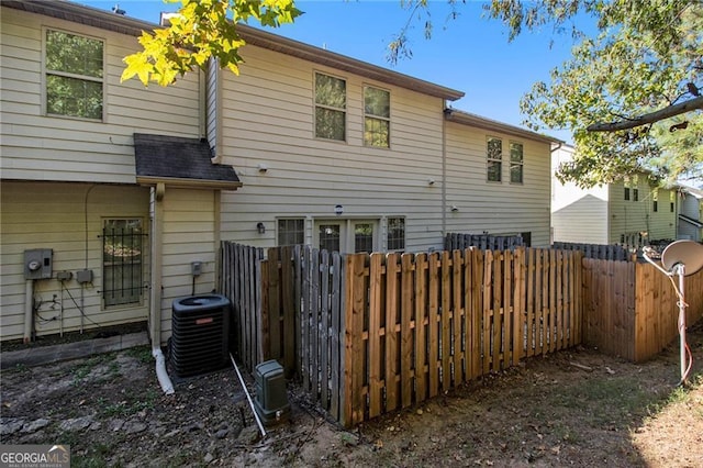 rear view of house with central AC unit, roof with shingles, and fence