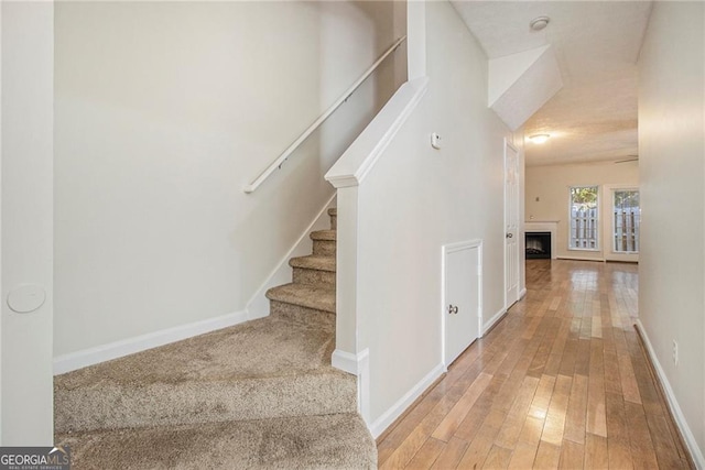 stairway featuring hardwood / wood-style flooring, a fireplace, and baseboards