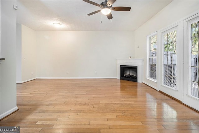 unfurnished living room featuring baseboards, a fireplace, a ceiling fan, and light wood-style floors