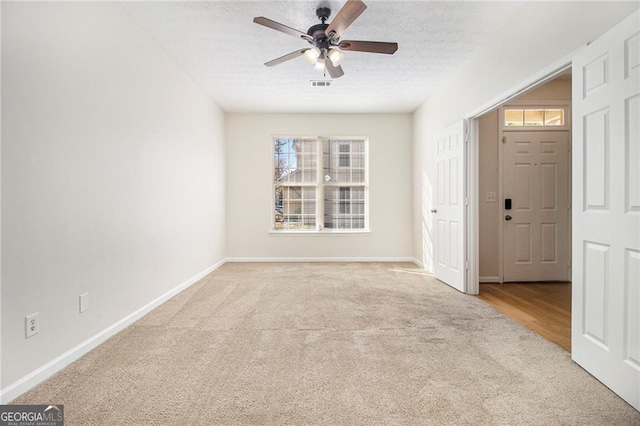 carpeted empty room with visible vents, a healthy amount of sunlight, a textured ceiling, and baseboards