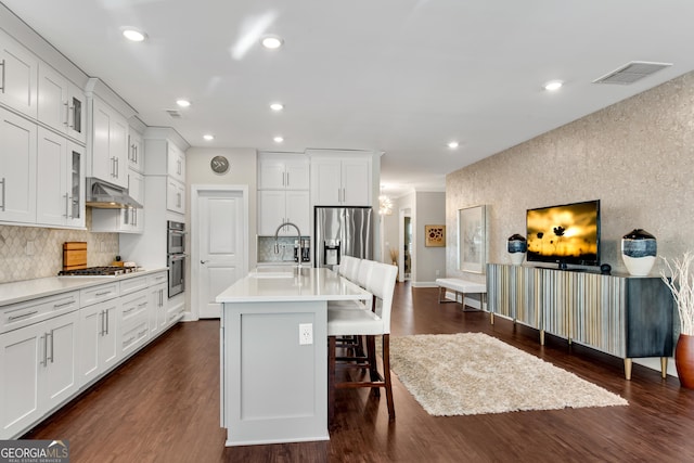 kitchen featuring appliances with stainless steel finishes, dark wood-style flooring, light countertops, under cabinet range hood, and a sink