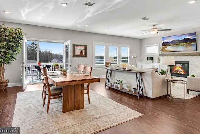 dining space with a glass covered fireplace, visible vents, baseboards, and wood finished floors