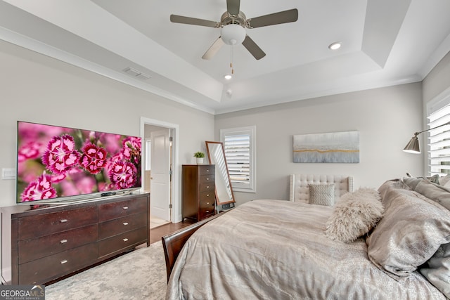 bedroom with a ceiling fan, a raised ceiling, visible vents, and multiple windows