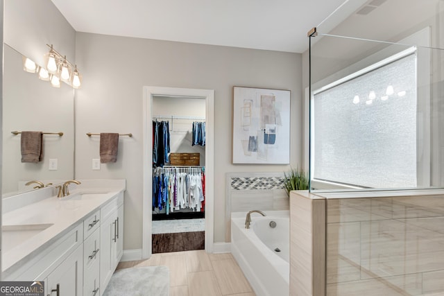 full bath with a walk in closet, a garden tub, double vanity, a sink, and baseboards