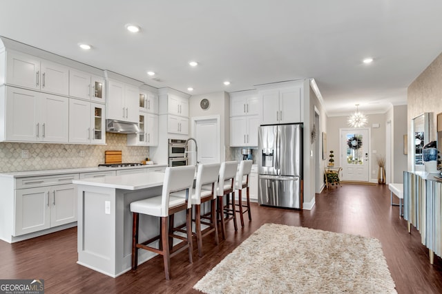 kitchen featuring a center island with sink, stainless steel appliances, tasteful backsplash, white cabinets, and under cabinet range hood