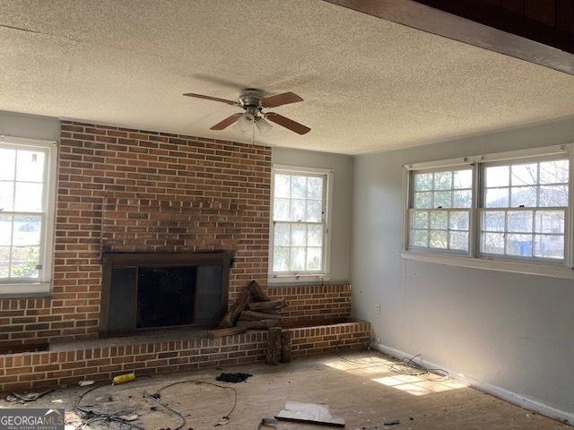 unfurnished living room featuring a textured ceiling, ceiling fan, and a fireplace