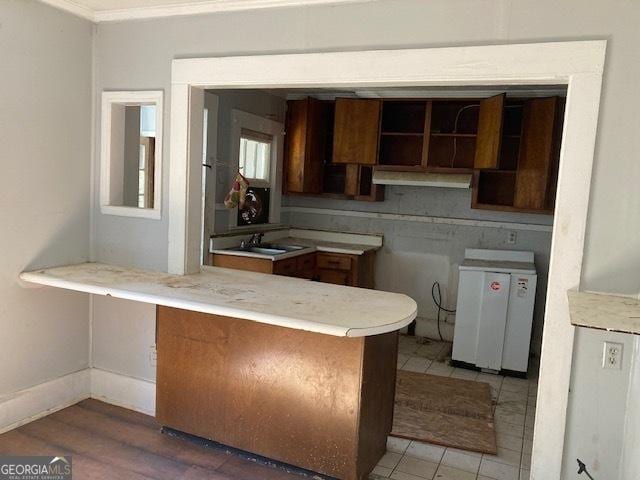 kitchen with baseboards, a peninsula, light countertops, crown molding, and a sink