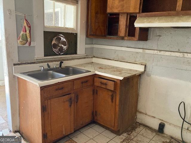 kitchen featuring brown cabinets, light tile patterned floors, light countertops, a sink, and exhaust hood