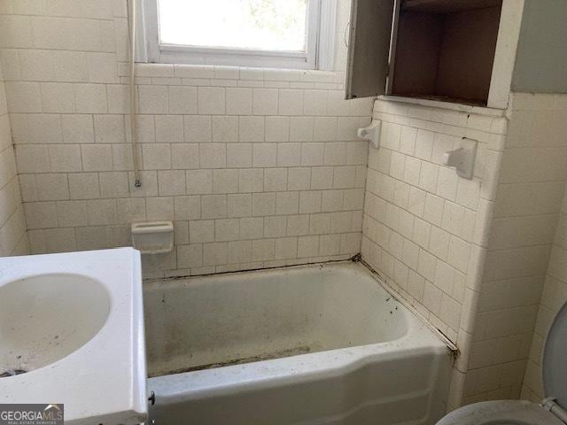 full bath featuring a bathtub, tile walls, and toilet