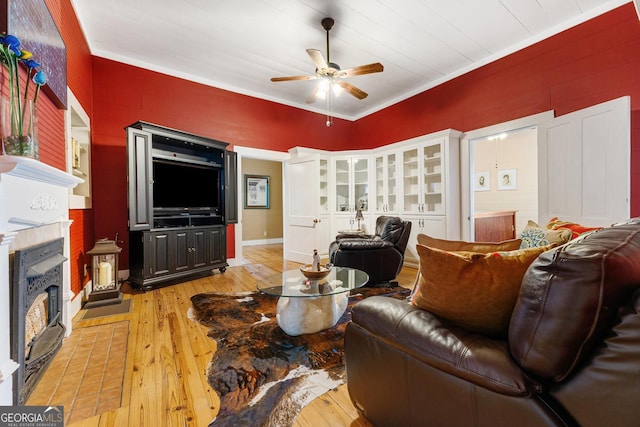 living room featuring light wood-style floors, a fireplace, ceiling fan, and crown molding