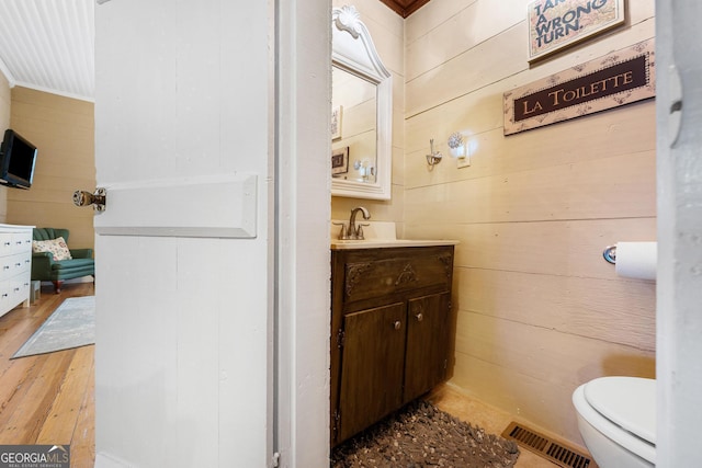 bathroom with toilet, wood walls, wood finished floors, vanity, and visible vents