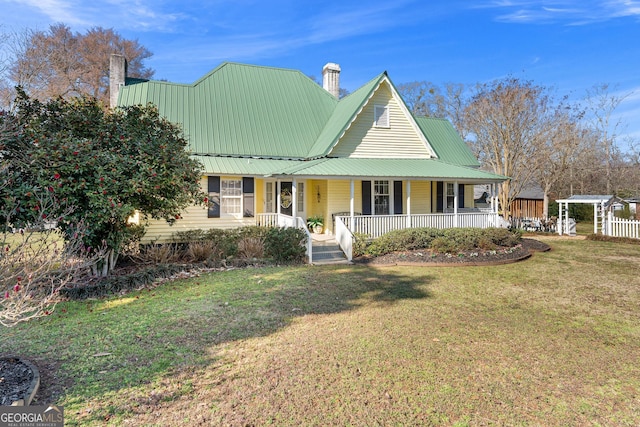 country-style home with a porch, a front yard, metal roof, and a chimney