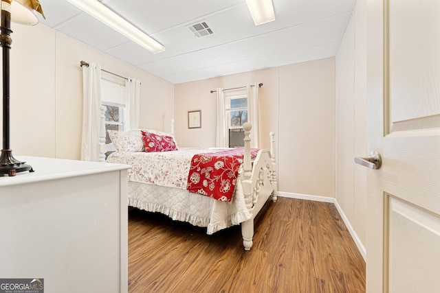 bedroom with multiple windows, wood finished floors, visible vents, and baseboards