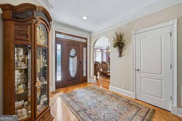 foyer entrance with baseboards, visible vents, arched walkways, crown molding, and light wood-style floors