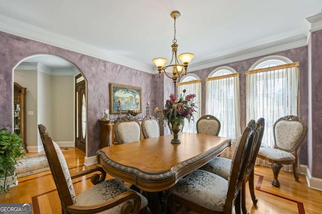 dining room featuring baseboards, arched walkways, light wood-style flooring, crown molding, and a notable chandelier