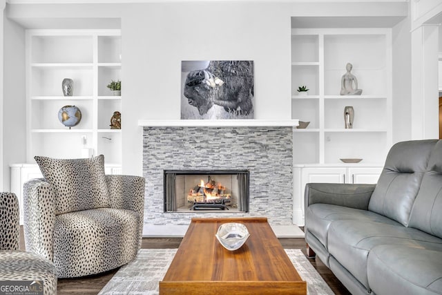 living area with built in features, dark wood-type flooring, and a warm lit fireplace