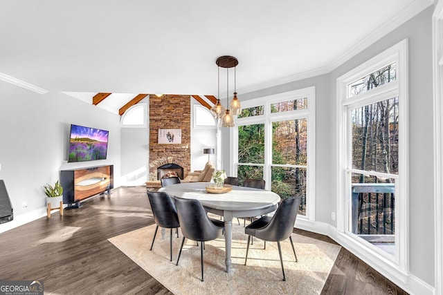 dining area with wood finished floors, baseboards, a fireplace, vaulted ceiling, and crown molding