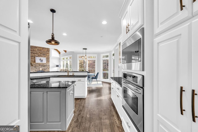 kitchen featuring a peninsula, a sink, hanging light fixtures, stainless steel appliances, and white cabinetry