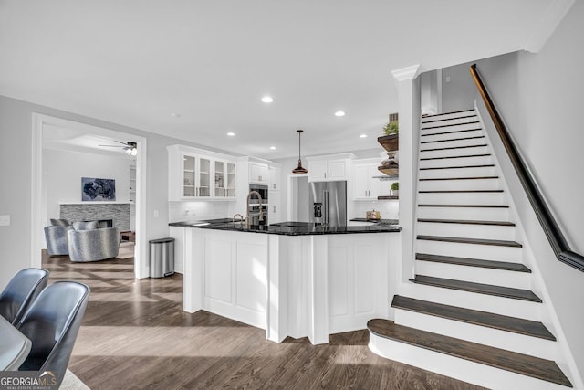 kitchen featuring dark wood finished floors, appliances with stainless steel finishes, white cabinets, a fireplace, and glass insert cabinets