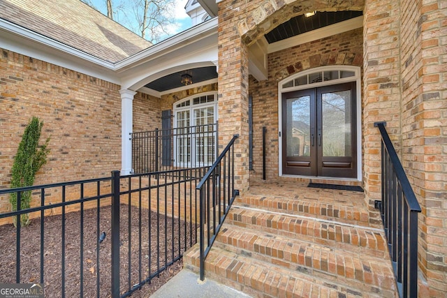 entrance to property featuring french doors, brick siding, and a shingled roof