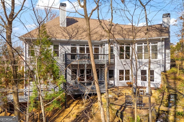 back of house with roof with shingles, a deck, a chimney, and fence