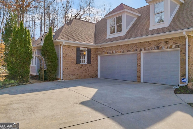 view of front facade with an attached garage, brick siding, roof with shingles, and driveway