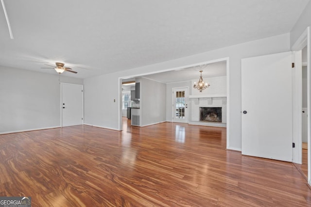 unfurnished living room with a brick fireplace, baseboards, wood finished floors, and ceiling fan with notable chandelier